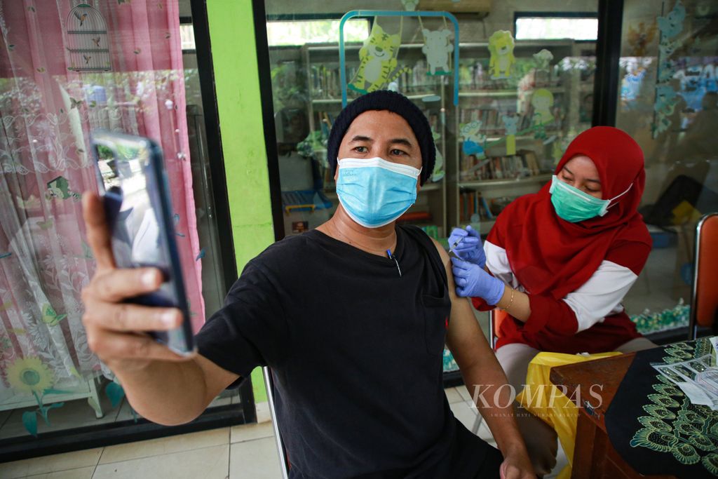 Warga berswafoto saat menerima suntikan vaksin Covid-19 dosis ketiga atau penguat di RPTRA Gondangdia, Jakarta Pusat, Senin (28/3/2022). Vaksinasi dosis lengkap dan satu kali <i>booster, </i>syarat agar bisa mudik Lebaran, telah meningkatkan minat warga.