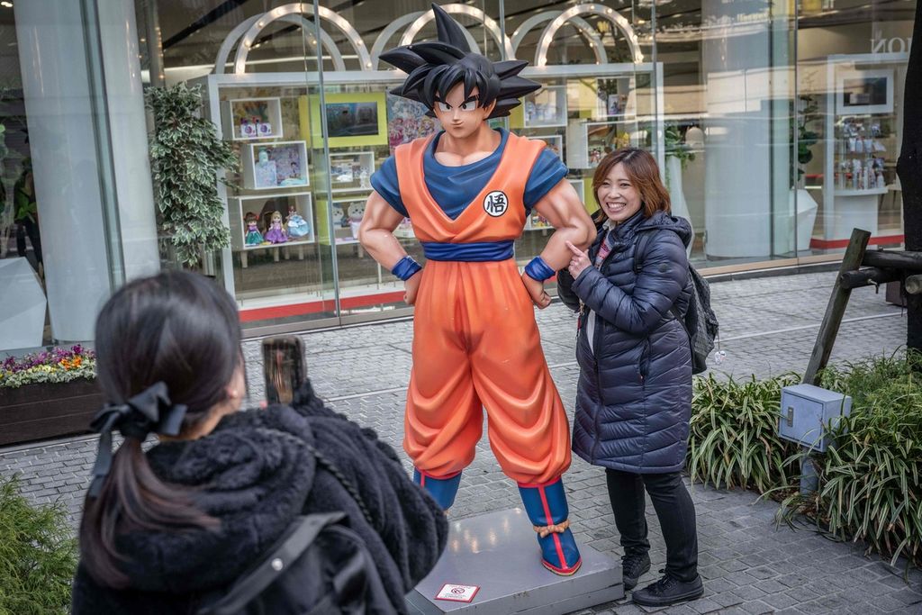 Seorang perempuan berpose untuk difoto di dekat patung tokoh Son Goku dalam manga <i>Dragon Ball</i> di Tokyo, Jepang, Jumat (8/3/2024). 