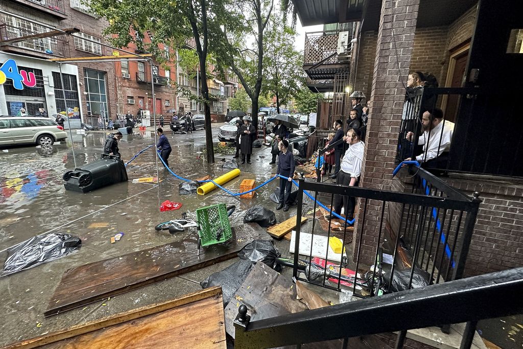 Warga menyaksikan pekerja berupaya membersihkan saluran air di perairan banjir, Jumat (29/9/2023), di Brooklyn, New York, Amerika Serikat. 