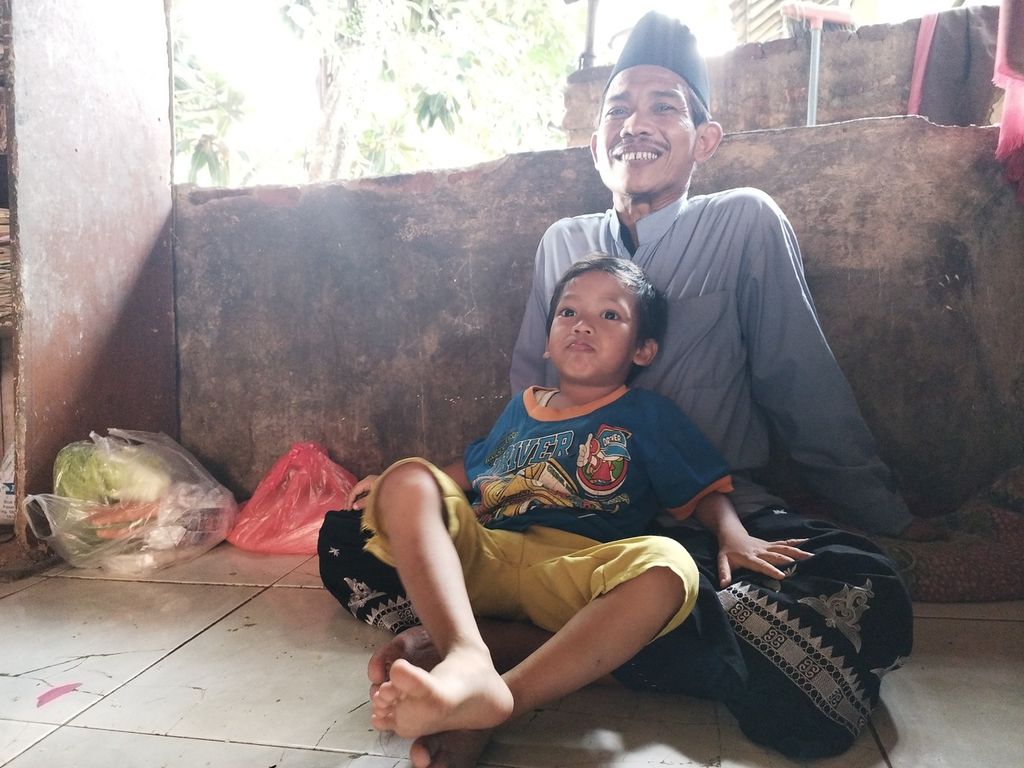 Asnawi (49) tengah memangku anaknya di teras rumahnya di Desa Cibarusahjaya, Kecamatan Cibarusah, Kabupaten Bekasi, Jawa Barat, Jumat (7/4/2023).