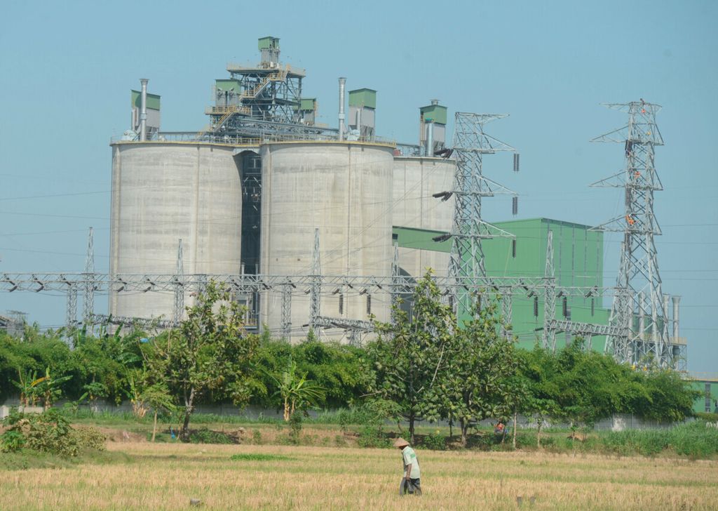Petani beraktivitas di lahan sawahnya dengan latar belakang bangunan pabrik semen di Desa Sugihmanik, Kecamatan Tanggungharjo, Kabupaten Grobogan, Jawa Tengah, Senin (14/9/2020). 