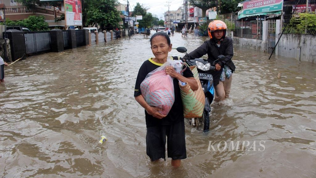 Warga berupaya melewati titik banjir yang ada di kawasan Sekip Jaya, Kecamatan Kemuning, Kota Palembang, Selasa (13/11/2018). 