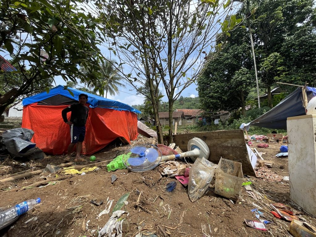 Penyintas gempa Cianjur, Dede Ramlan, berdiri di depan tenda yang masih tersisa setelah banjir pada Senin (20/3/2023)