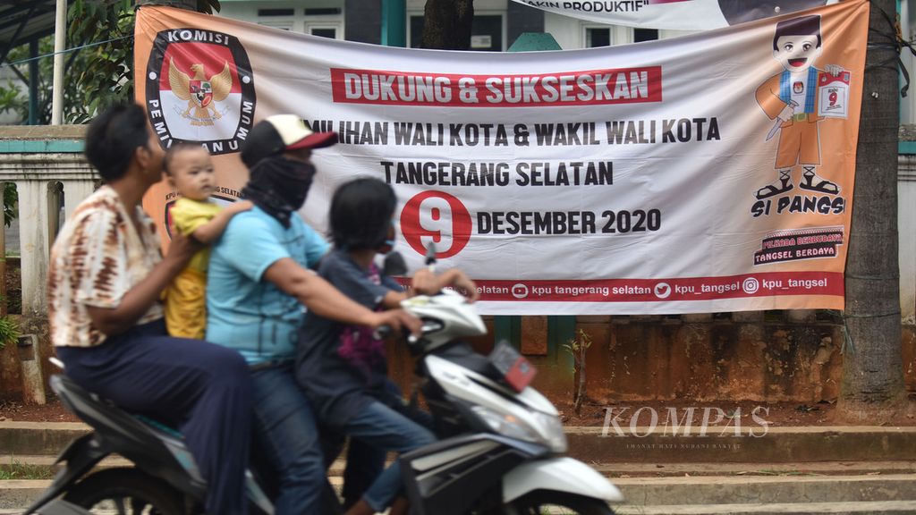 Warga melintasi spanduk sosialisasi pelaksanaan Pemilihan Kepala Daerah (Pilkada) Kota Tangerang Selatan di Jalan Pondok Aren, Tangerang Selatan, Banten, Sabtu (25/7/2020). 