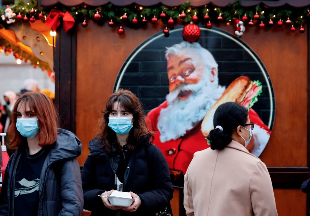 Pengunjung yang memakai masker berjalan melewati kios-kios di pasar natal di pusat kota London, Inggris, Sabtu (18/12/2021). 