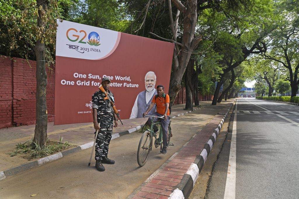 Seorang anggota paramiliter India berdiri di depan baliho KTT G20, sementara seorang pesepeda melintas di dekatnya, di New Delhi, India, Jumat (8/9/2023). 