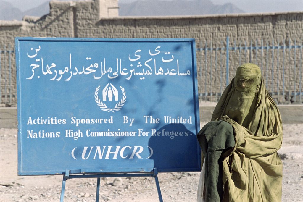 Seorang perempuan yang mengenakan burqa seperti diwajibkan Taliban, berjalan melewati plang bertuliskan UNHCR pada 11 November 1996. Dia hendak mengambil bantuan selimut dan pakaian hangat yang diberikan oleh program distribusi bantuan musim dingin.  