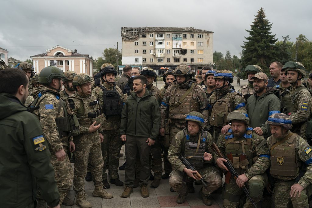 Presiden Ukraina Volodymyr Zelenskyy (tengah) berdiri bersama tentara Ukraina seusai upacara pemasangan bendera di wilayah yang baru mereka rebut lagi dari pasukan Rusia di Izium, Ukraina, 14 September 2022.  