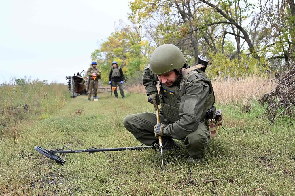Anggota penjinak bom pasukan Garda Nasional Ukraina memeriksa ranjau di sebuah jalan tanah di dekat posisi area pasukan Ukraina yang ditinggalkan di wilayah utara Kharkiv, Ukraina, Selasa (20/9/2022). 