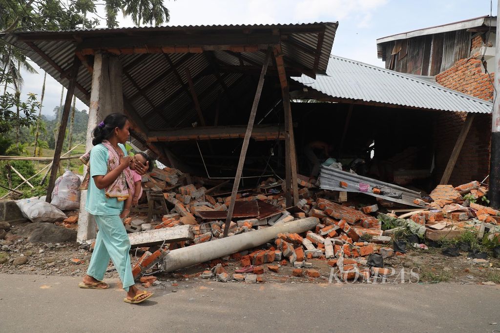 Warga melintas di depan rumah yang ambruk karena gempa di Jorong Satu Sipa Rayo, Nagari Malampah, Kecamatan Tigo Nagari, Kabupaten Pasaman, Sumatera Barat, Minggu (27/2/2022). 