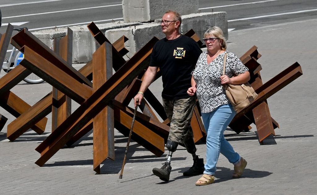 A disabled man, veteran of the war with Russia, wearing a T-shirt with the emblem of the 20th Oktyrka motorized infantry battalion, walks with a woman past anti-tank Czech hedgehogs or crosses, in the center of Ukrainian capital of Kyiv on June 22, 2022.