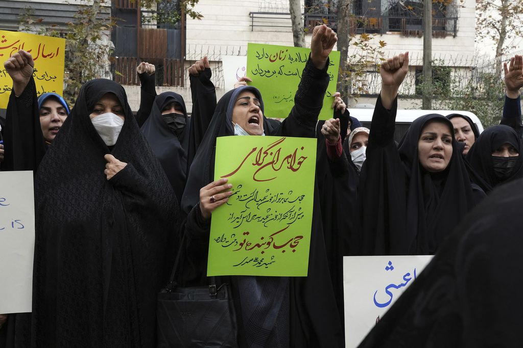 Sekelompok demonstran propemerintah meneriakkan slogan-slogan ketika salah satu dari mereka memegang poster yang mendorong perempuan mengenakan jilbab di depan kantor PBB di Teheran, Iran, Selasa (13/12/2022). 