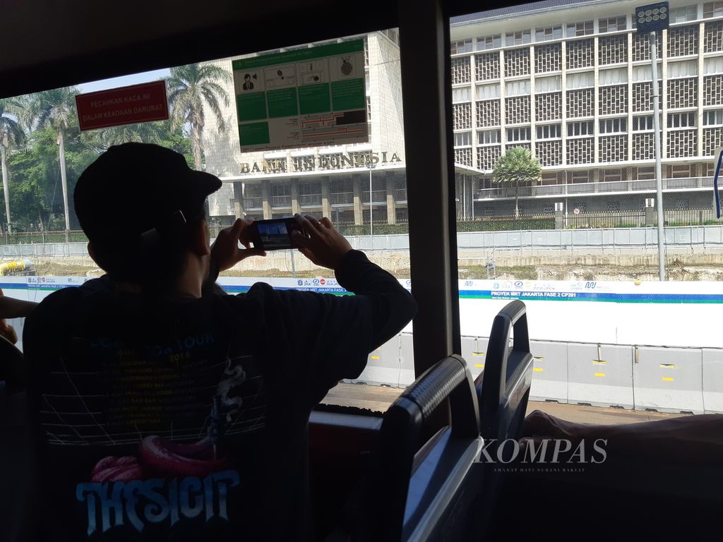 Seorang penumpang Bus Wisata Transjakarta sedang mengabadikan Gedung Bank Indonesia di Jalan MH Thamrin, Jakarta Pusat, Minggu (14/4/2024). Obyek ini menjadi titik tujuan wisata pada penjelajahan Jakarta. Bus wisata ini diminati pelancong domestik ataupun internasional.