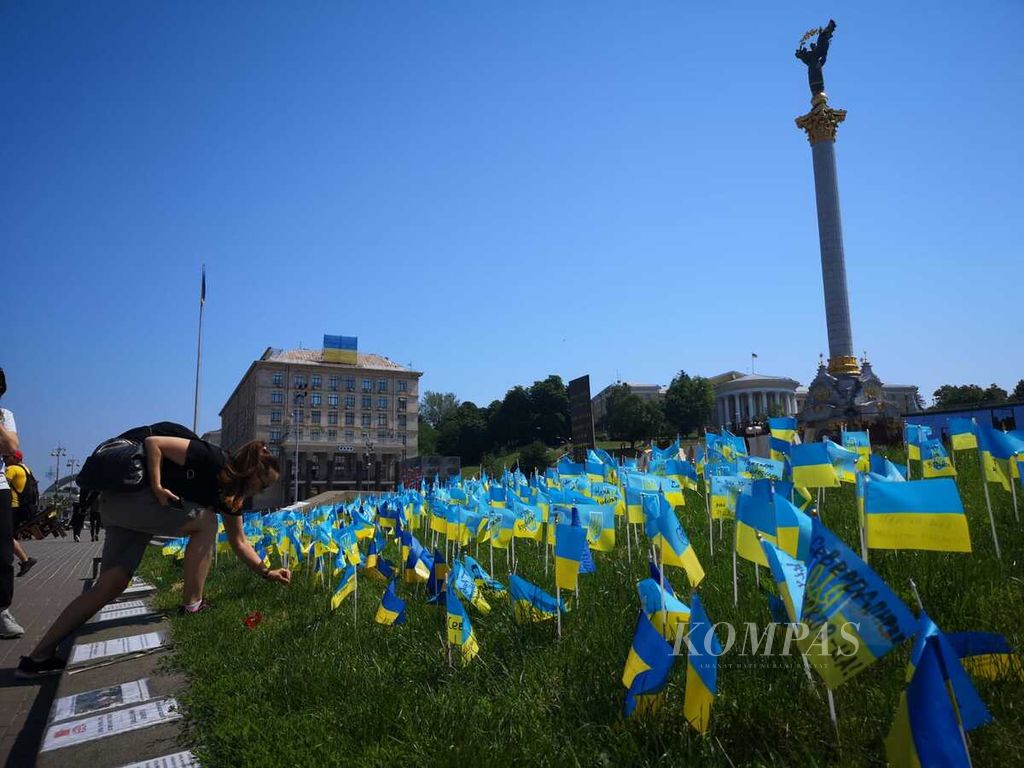 Warga memegang salah satu replika bendera Ukraina yang ditancapkan di dekat Maidan Plaza, Kyiv, Ukraina, Minggu (12/6/2022). 