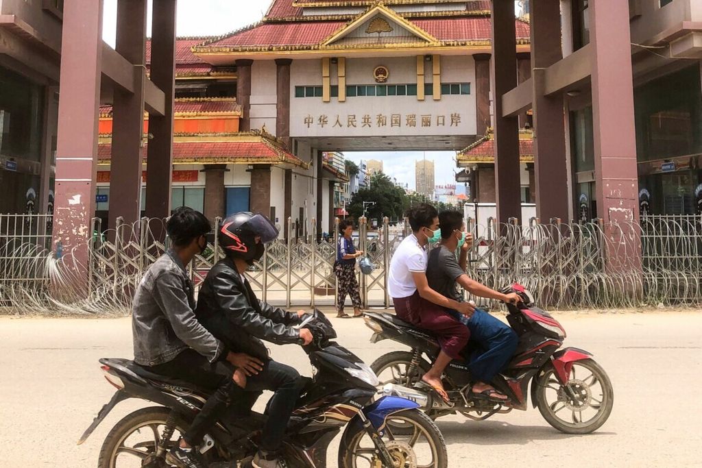 Para pengendara motor di Muse, Negara Bagian Shan, Myanmar, melewati gerbang perbatasan Myanmar dengan Ruili, Provinsi Yunnan, China, pada 5 Juli 2021.  