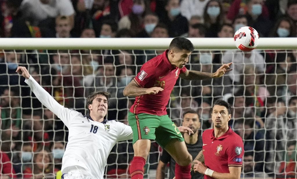 Bek Portugal Joao Cancelo (tengah) menyundul bola saat dibayangi penyerang Serbia Dusan Vlahovic (kiri) dalam lanjutan kualifikasi Piala Dunia 2022 zona Eropa grup A di Stadion Luz, Lisabon, Portugal, Senin (15/11/2021) dini hari WIB. 