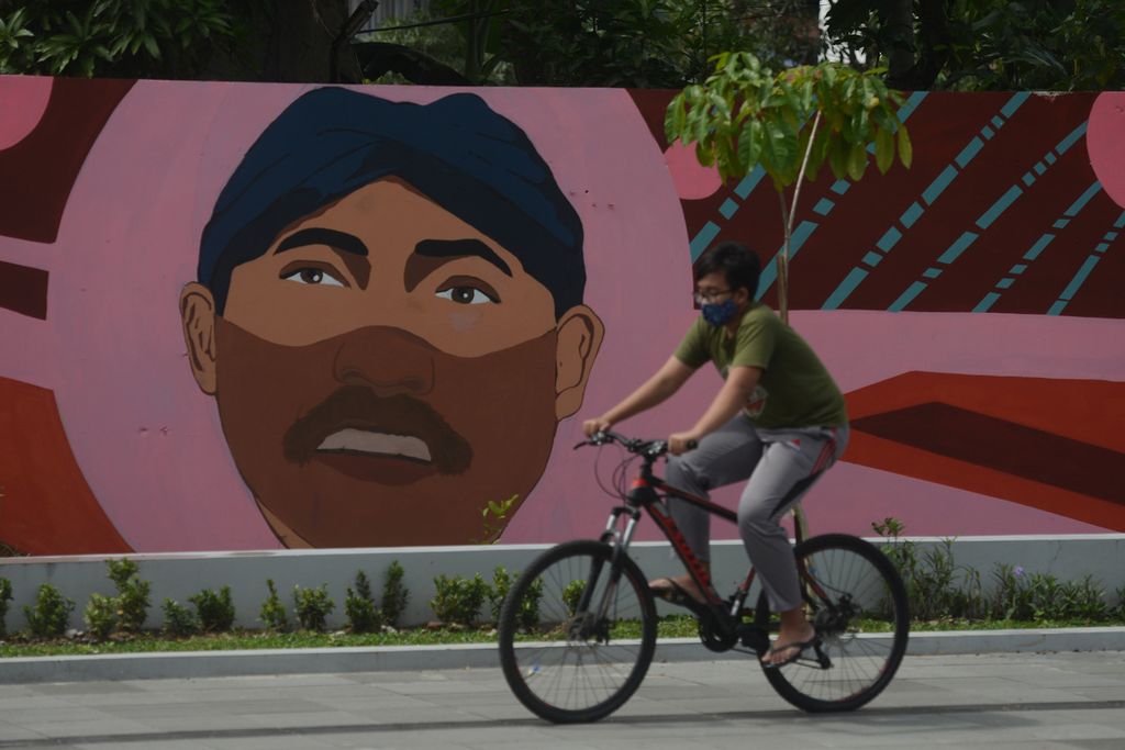 Pesepeda melintas di depan mural bergambar sosok mantan Wali Kota Surakarta FX Hadi Rudyatmo yang mengenakan masker di Jalan Ir Juanda, Surakarta, Jawa Tengah, Sabtu (13/2/2021). 
