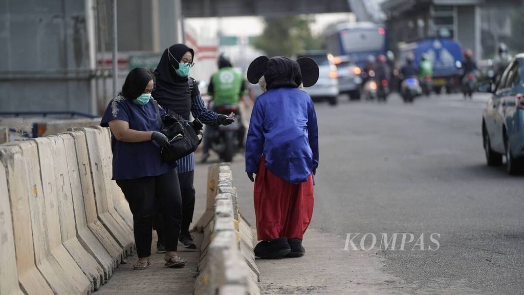 Pejalan kaki memberikan uang kepada badut Mickey Mouse yang berjalan gontai di Jalan MT Haryono, Jakarta Timur, Rabu (8/7/2020).