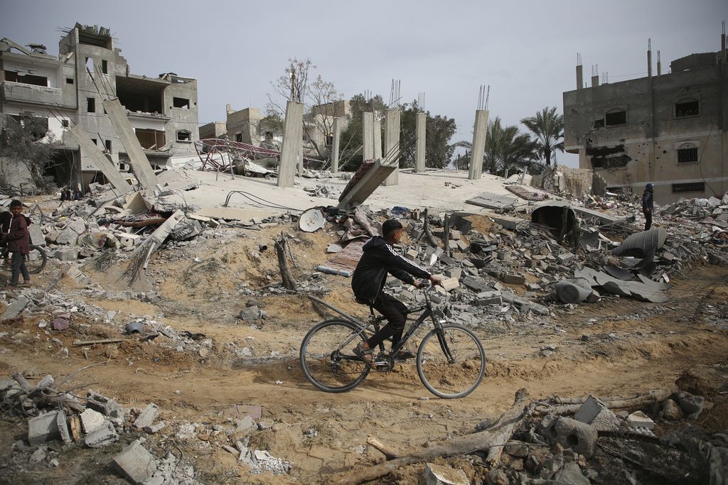 Seorang warga Palestina naik sepeda memeriksa puing-puing reruntuhan bangunan permukiman milik keluarga Abu Muammar seusai serangan udara Israel di Rafah, Jalur Gaza selatan, Jumat (29/3/2024). 