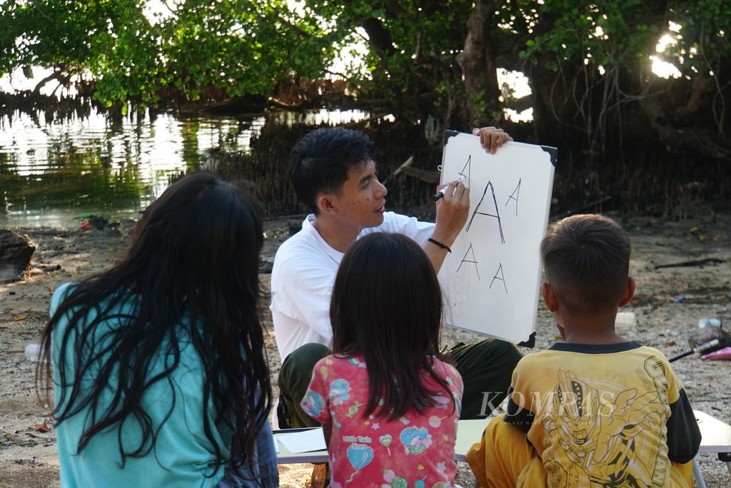 Farlan Erlangga (22) memperkenalkan alfabet kepada tiga anak yang belum mampu membaca, Sabtu (18/11/2023), di Pulau Bunaken, Manado, Sulawesi Utara. 