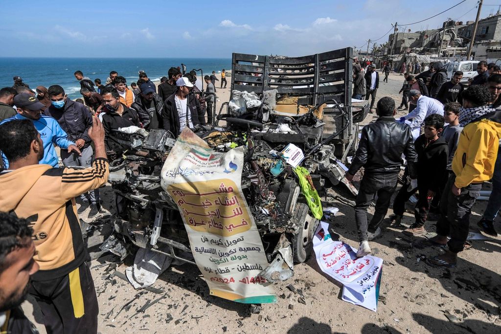 Warga Palestina berkerumun di dekat sebuah truk pengangkut bantuan kemanusiaan yang luluh lantak akibat, menurut laporan, serangan udara Israel di ruas jalan pinggir pantai di Deir El-Balah, Jalur Gaza tengah, Minggu (3/3/2024). 