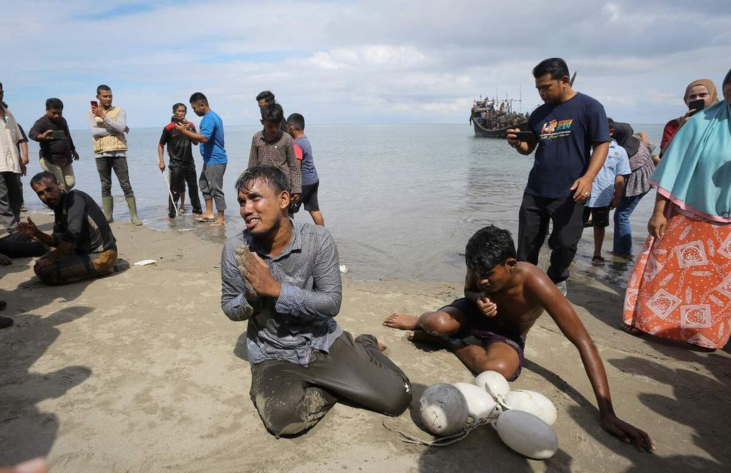 Pengungsi Rohingya terduduk di pantai setelah berenang dari kapal yang mengangkutnya, sementara para pengungsi lainnya masih berada di kapal saat kapal mereka ditolak masyarakat setempat di Pineung, Provinsi Aceh, Kamis (16/11/2023). Sebelum menolak kehadiran mereka, warga setempat memberi mereka makan dan air minum. 