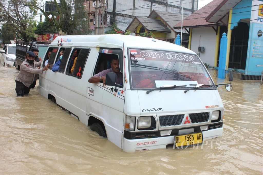 Personel polisi membantu mendorong sebuah mobil yang mogok karena terendam banjir di jalan nasional, Kota Lhoksukon, Kabupaten Aceh Utara, Provinsi Aceh, Senin (3/1/2022). Banjir di Aceh Utara menggenangi 14 kecamatan dengan jumlah desa sebanyak 108 desa. Jumlah warga yang mengungsi 24.332 orang dan sebanyak tiga warga meninggal dunia.