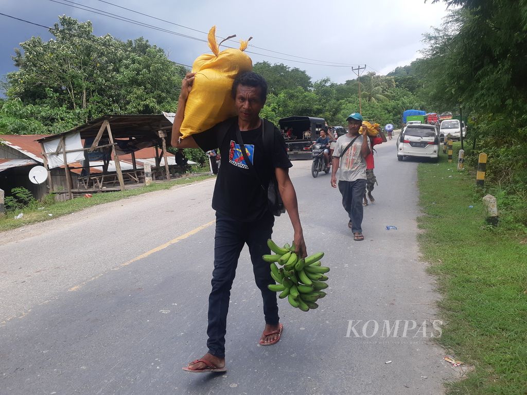Penumpang turun dari kendaraan, lalu memikul barang akibat longsor yang menutup Jalan Timor Raya di Kelurahan Takari, Kabupaten Kupang, NTT, Sabtu (18/2/2023).