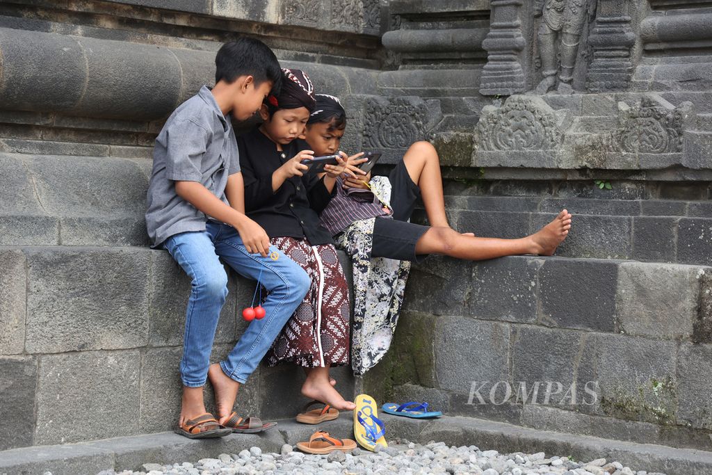 Anak-anak bermain lato-lato dan gawai sebelum mengikuti sembahyang untuk merayakan Galungan di Candi Prambanan, Sleman, DI Yogyakarta, Rabu (4/1/2023).