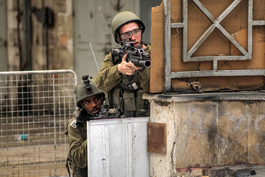 Dua anggota pasukan Israel mengintai dari balik tembok sambil bersiap menembakkan senjata yang dibawanya dalam operasi militer ke kota Jenin, Tepi Barat, Palestina, Selasa (4/7/2023). 