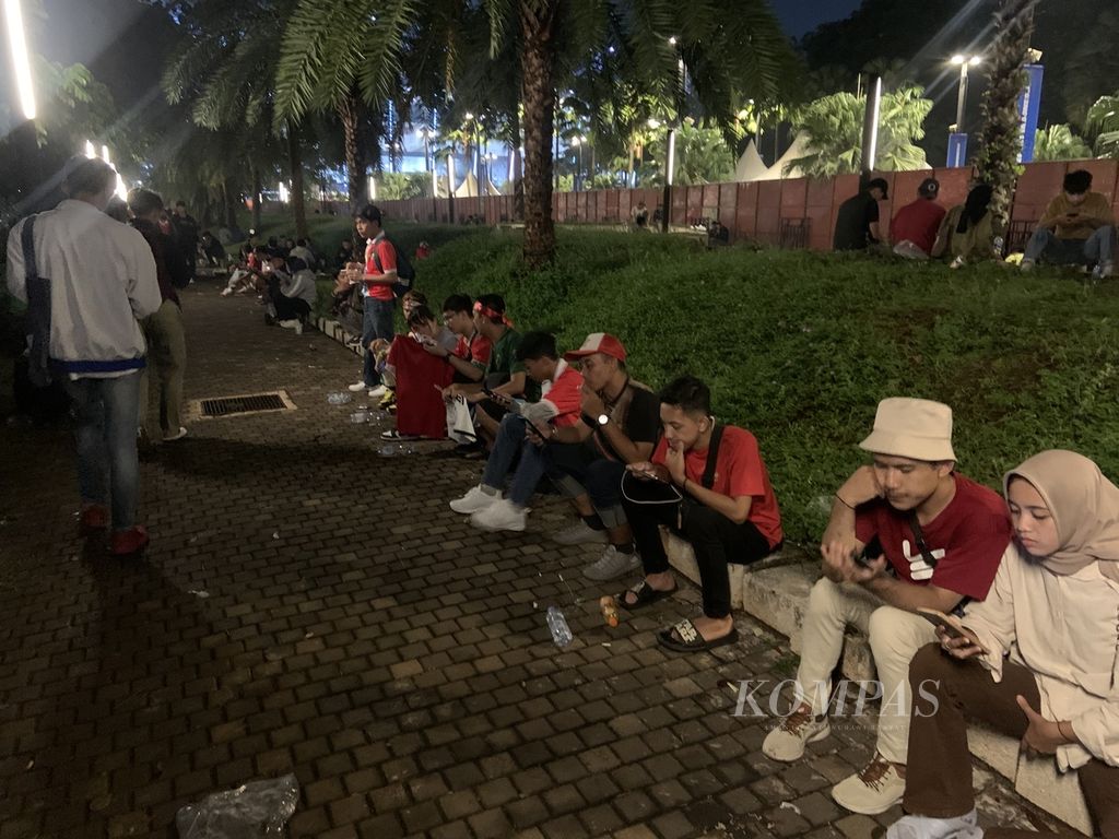 Para penonton yang tidak bertiket duduk di area luar Stadion Gelora Bung Karno, Jakarta, Senin (19/6/2023). Mereka cukup puas menikmati suasana laga persahabatan Indonesia lawan Argentina dari luar stadion.