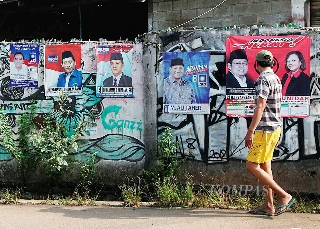 Warga melintas di depan poster caleg yang masih terpasang di salah satu sudut Kota Tangerang, Banten, Minggu (27/4/2019). Keberadaan poster caleg usai pencoblosan itu hanya menambah sampah di sudut-sudut kota. 