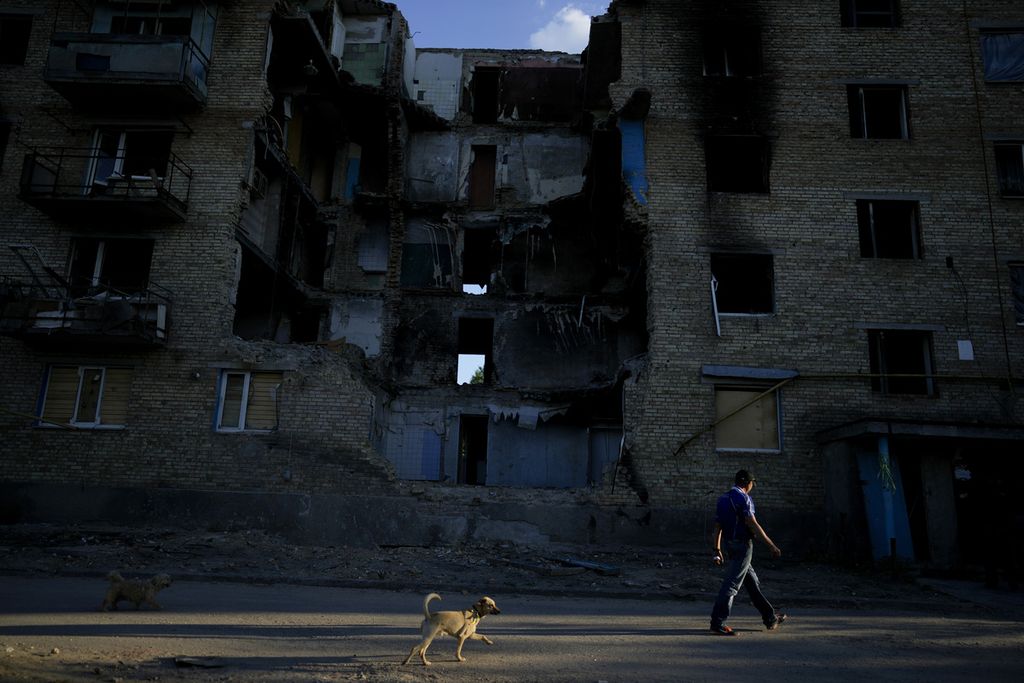 Seorang warga berjalan bersama anjing miliknya melewati bangunan apartemen yang rusak akibat serbuan senjata Rusia di pinggiran ibu kota Kyiv, Ukraina, Rabu (8/6/2022). Negara-negara Barat sekutu Ukraina terlihat mulai menggeser pandangannya soal perang karena dampaknya terhadap kondisi di dalam negeri. 