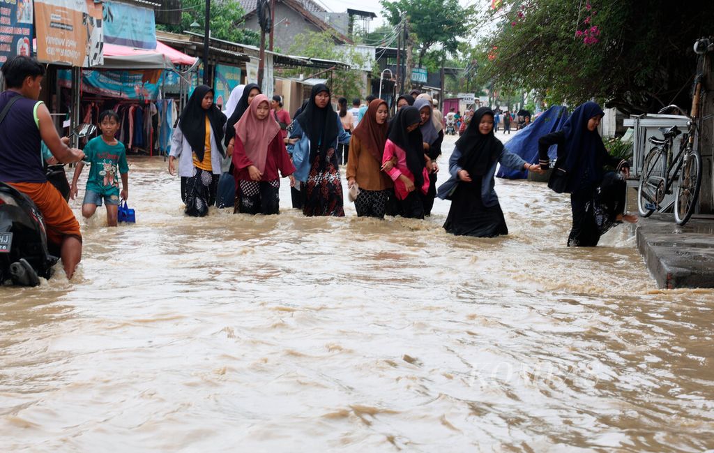 Santriwati yang menghentikan aktivitas belajar mereka saat melintasi banjir di Kecamatan Gubug, Kabupaten Grobogan, Jawa Tengah, Selasa (6/2/2024).