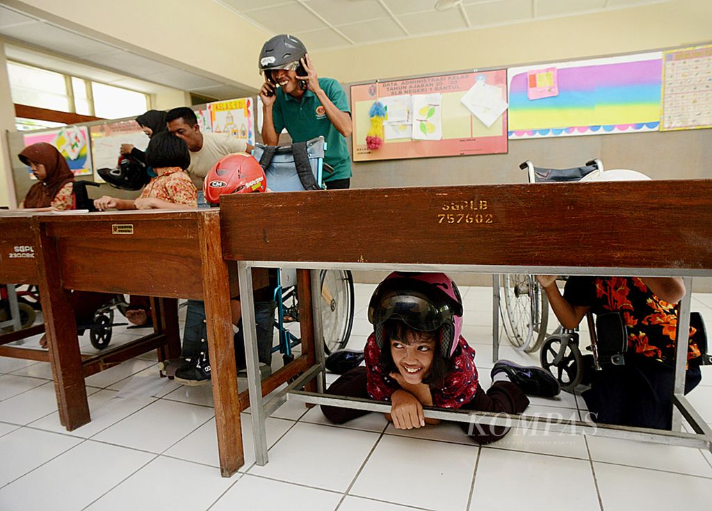 Murid tunadaksa mengenakan helm dan berlindung di bawah meja saat kegiatan simulasi penyelamatan dari bencana alam di SLB Negeri 1 Bantul, Kecamatan Kasihan, Bantul, DI Yogyakarta, akhir Januari 2016. 