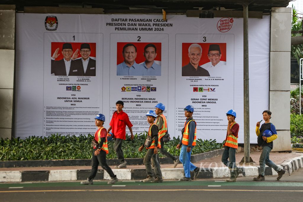 Pekerja proyek melintasi spanduk pasangan calon presiden dan calon wakil presiden pada Pemilu 2024 di kawasan Kuningan, Jakarta, Selasa (16/1/2024). Pemasangan spanduk ini bertujuan untuk menyosialisasikan visi misi mereka kepada masyarakat.