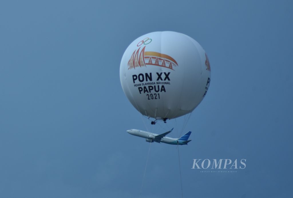 Pesawat Garuda Indonesia melewati balon udara PON Papua 2021 tepat di atas arena perlombaan cabang atletik di Stadion Atletik Mimika, Kota Timika, Kabupaten Mimika, Kamis (14/10/2021).