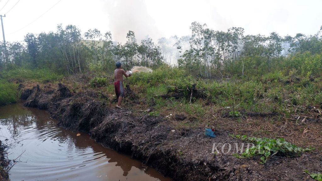 Warga berupaya menyiram gambut yang terbakar di dekat tempat tinggalnya di Kecamatan Gambut, Kabupaten Banjar, Kalimantan Selatan, Sabtu (30/9/2023).