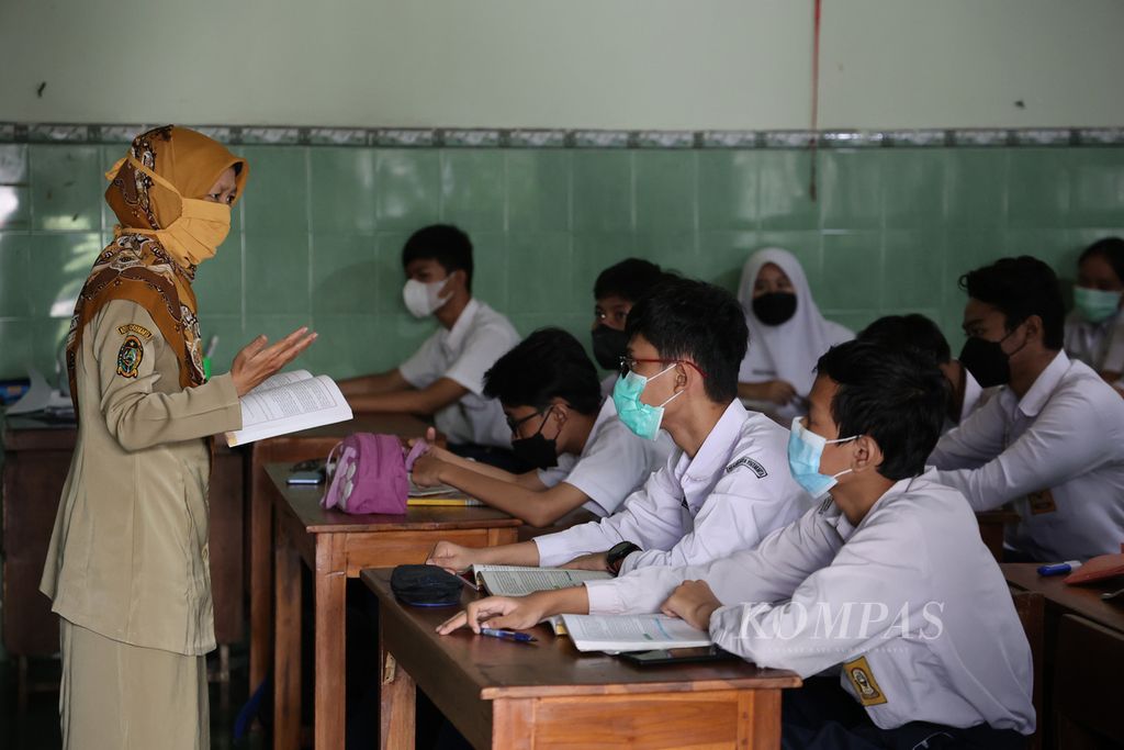 Guru menyampaikan materi ajar kepada murid pada hari pertama penerapan pertemuan tatap muka (PTM) 100 persen di SMP Negeri 2 Yogyakarta, Yogyakarta, Senin (24/1/2022). 