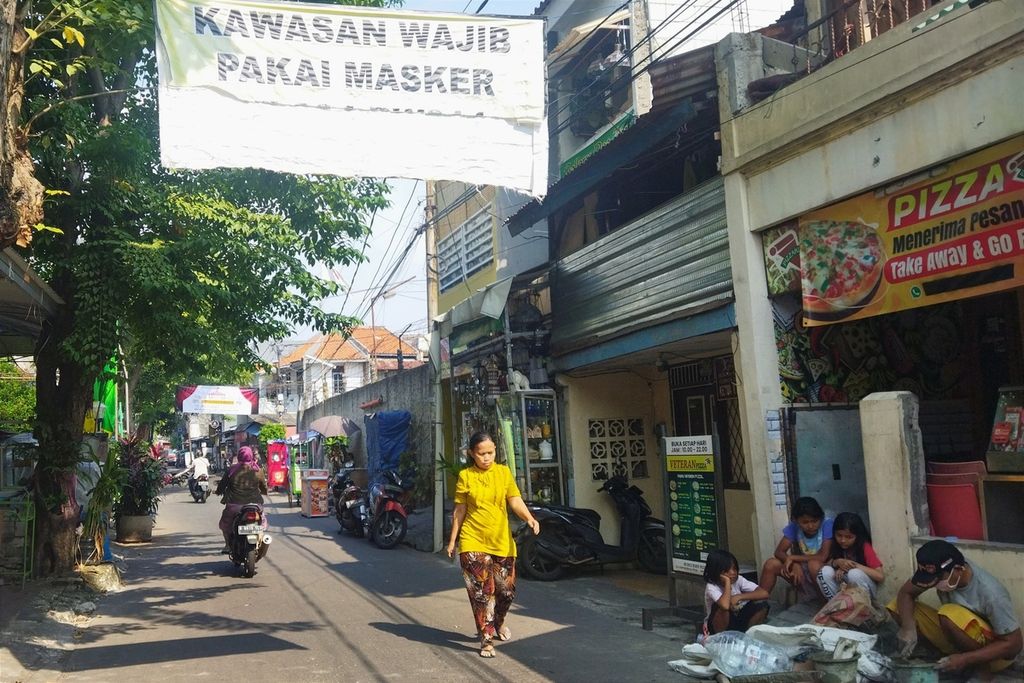 Warga melintas di bawah spanduk bertuliskan kawasan wajib pakai masker di Jalan Kemandoran Pluis, Grogol Utara, Kebayoran Lama, Jakarta Selatan, Selasa (12/7/2022).