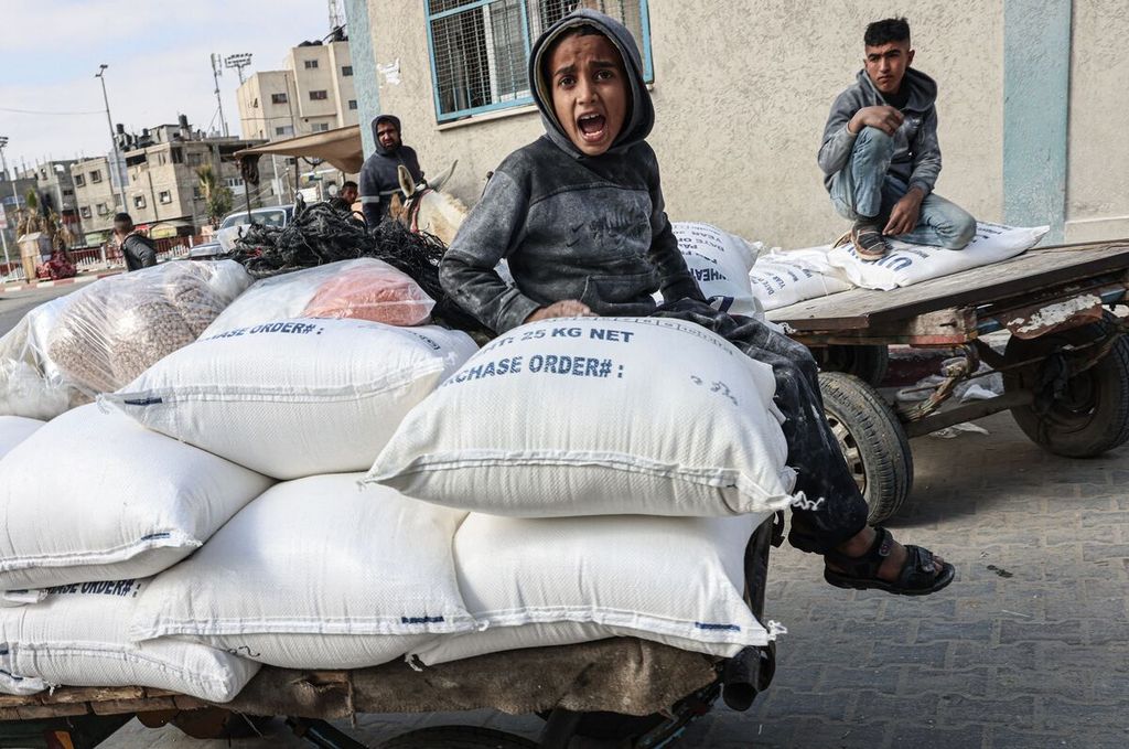 Seorang anak Palestina duduk di atas kantong-kantong berisi gandum yang diberikan untuk keluarga-keluarga miskin di pusat penyaluran UNRWA di kamp pengungsi Rafah, Jalur Gaza selatan, 22 Januari 2023. 