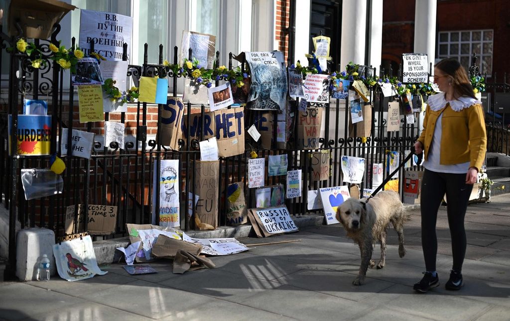 Seorang pejalan kaki melewati berbagai poster, gambar, dan coretan pesan berisi ungkapan menentang serangan Rusia ke Ukraina yang dipajang di sebuah pagar di seberang Kedutaan Rusia untuk Inggris di London, Inggris, 18 Maret 2022. 
