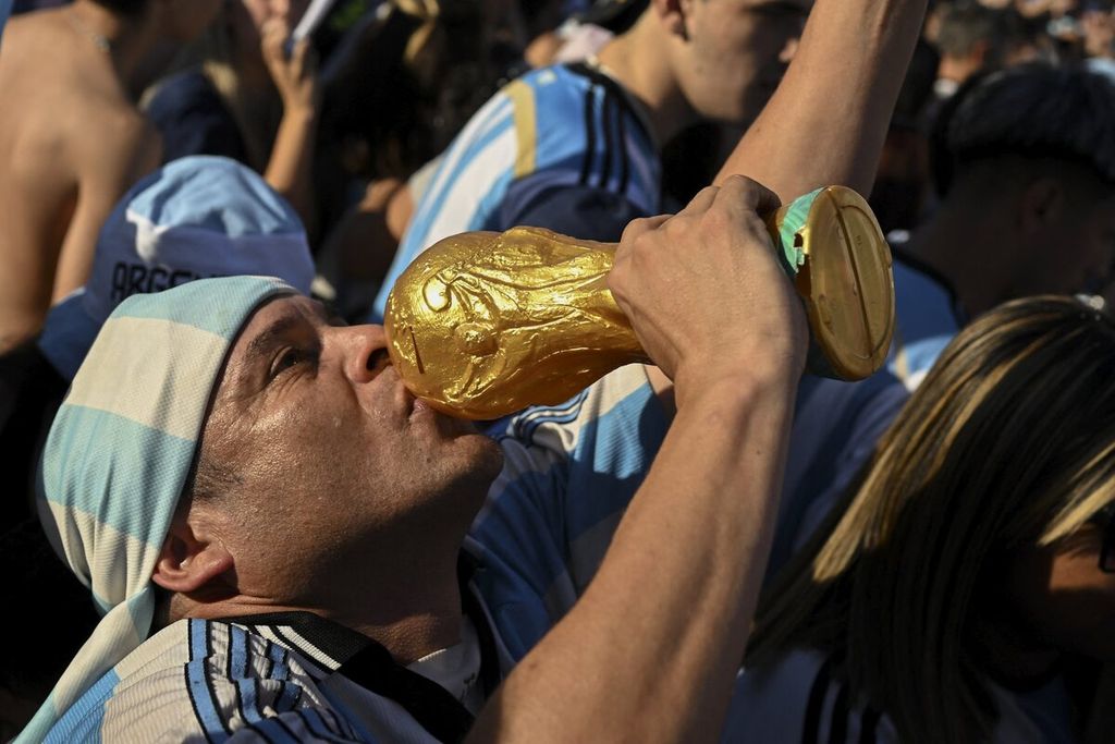 Pendukung Argentina di Buenos Aires mencium replika trofi Piala Dunia saat merayakan kemenangan tim kesayangannya atas Kroasia pada semifinal Piala Dunia Qatar 2022, Selasa (13/12/2022). 