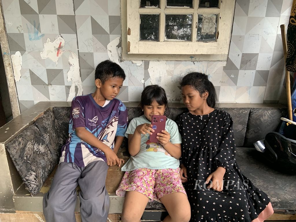 Dewi Sekartadji (8), bersama dua temannya, Ihza (kiri) dan Aisyah (kanan), di teras rumah, menikmati konten-konten hiburan di platform Tiktok, Selasa (19/9/2023), Sepulang sekolah, para pelajar SD itu kerap menghabiskan waktu untuk beristirahat sore sembari mencari hiburan di media sosial. Konten-konten yang disukai Dewi di antaranya musik dan parodi komedi
