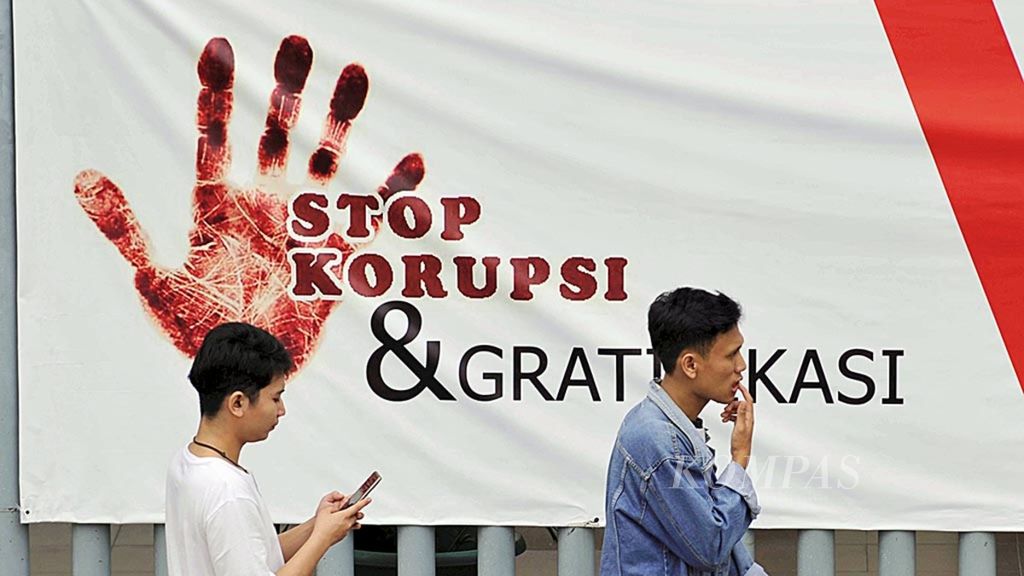 Warga melintas di depan spanduk bertuliskan ”Stop Korupsi & Gratifikasi”, Kamis (13 September 2018), di Jalan MH Thamrin, Jakarta. Kata <i>melintas</i> dapat dipilih untuk menggantikan kata <i>melintasi</i> yang sering keliru digunakan.