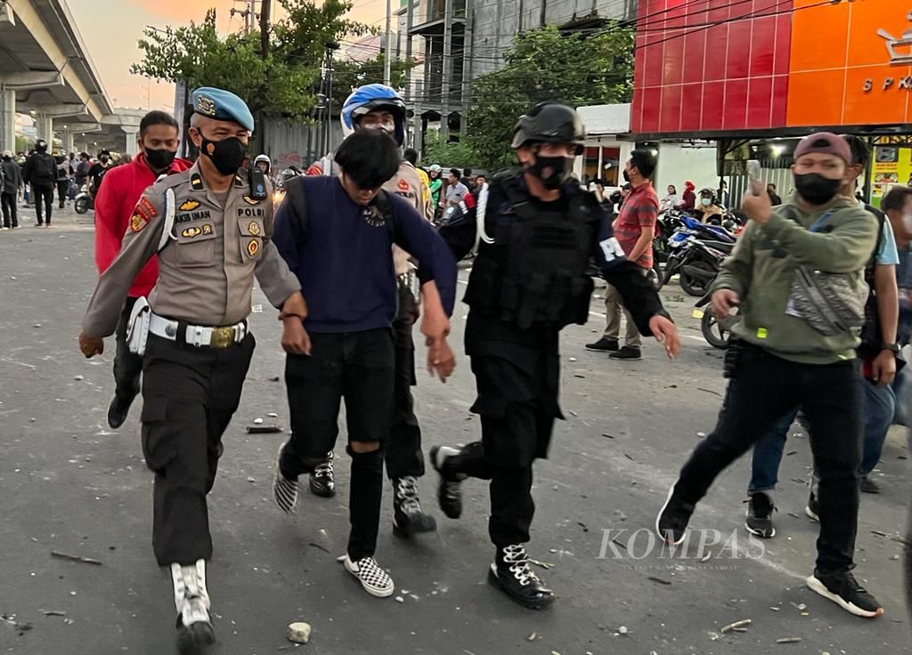 Polisi membawa seorang peserta unjuk rasa untuk diamankan seusai aksi berujung ricuh di Makassar, Senin (11/4/2022).