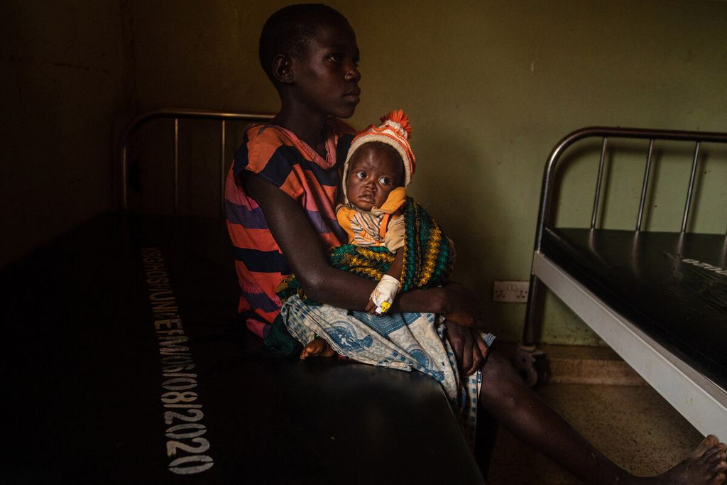 Ruth Abbo (9) memangku saudara perempuannya yang berusia empat tahun yang kekurangan gizi karena mereka terdampar setelah ibu mereka meninggalkan mereka di rumah sakit Kaabong di Kaabong, wilayah Karamoja, Uganda, Rabu (25/5/2022). 