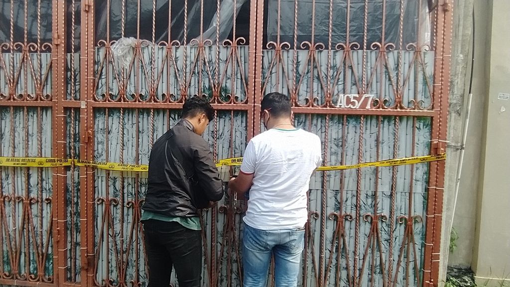 Polisi berpakaian preman tengah memasang gembok di pintu gerbang rumah keluarga korban di kompleks Citra Garden 1, Kalideres, Jakarta Barat, Senin (14/11/2022).