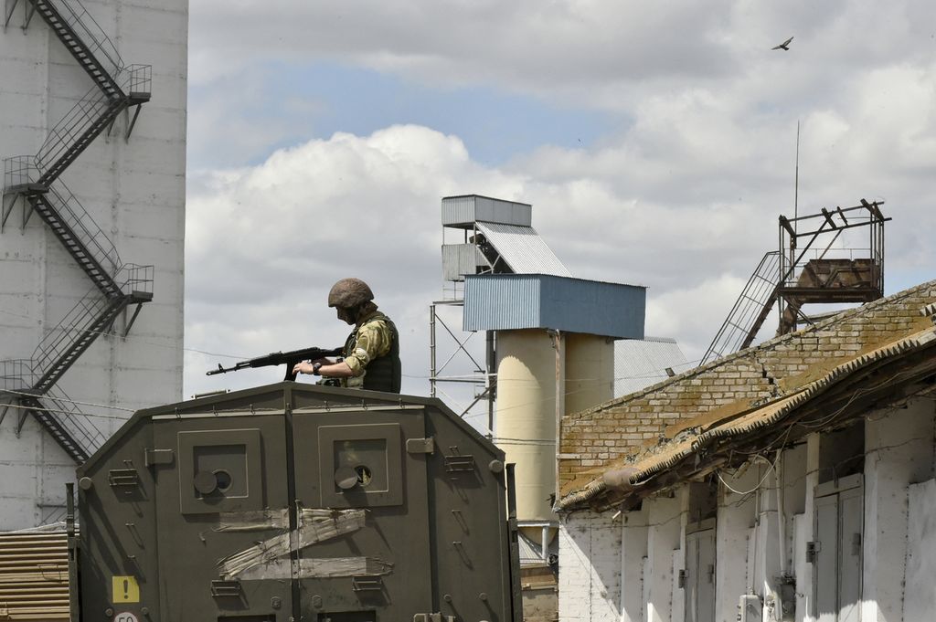 Seorang anggota militer Rusia berdiri di atas kendaraan tempur sambil memegang senjata mengawasi sebuah silo tempat penyimpanan gandum Ukraina di Melitopol, wilayah Zaporizhia, 14 Juli 2022. 