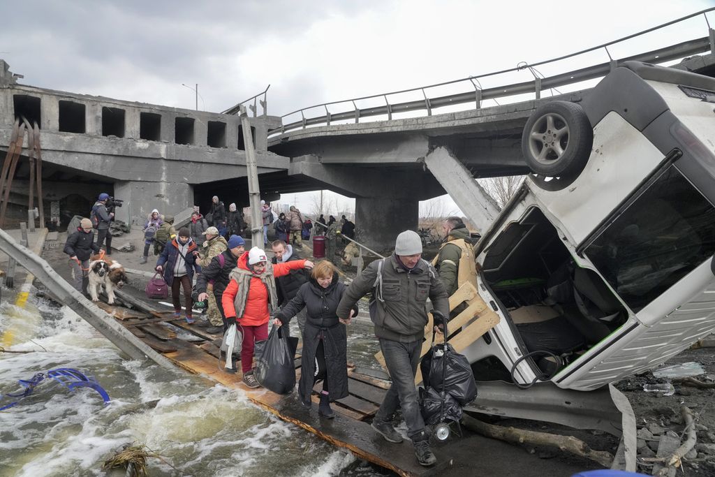 Warga menyeberangi lewat jalan darurat yang dibangun di bawah sebuah jembatan yang luluh lantak saat mereka mengungsi dari kota Irpin, dekat Kiev, Ukraina, Senin (7/3/2022). 